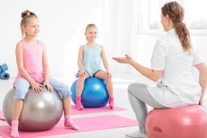 Young physiotherapist explaining exercises to smiling school girls sitting on exercise balls