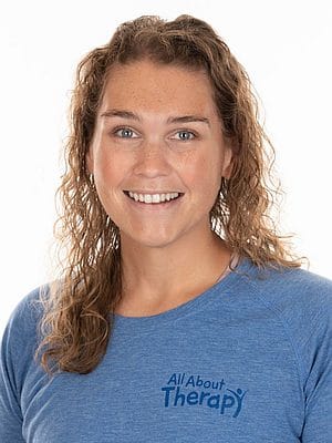 Smiling woman in blue All About Therapy t-shirt with curly hair, promoting pediatric therapy services.